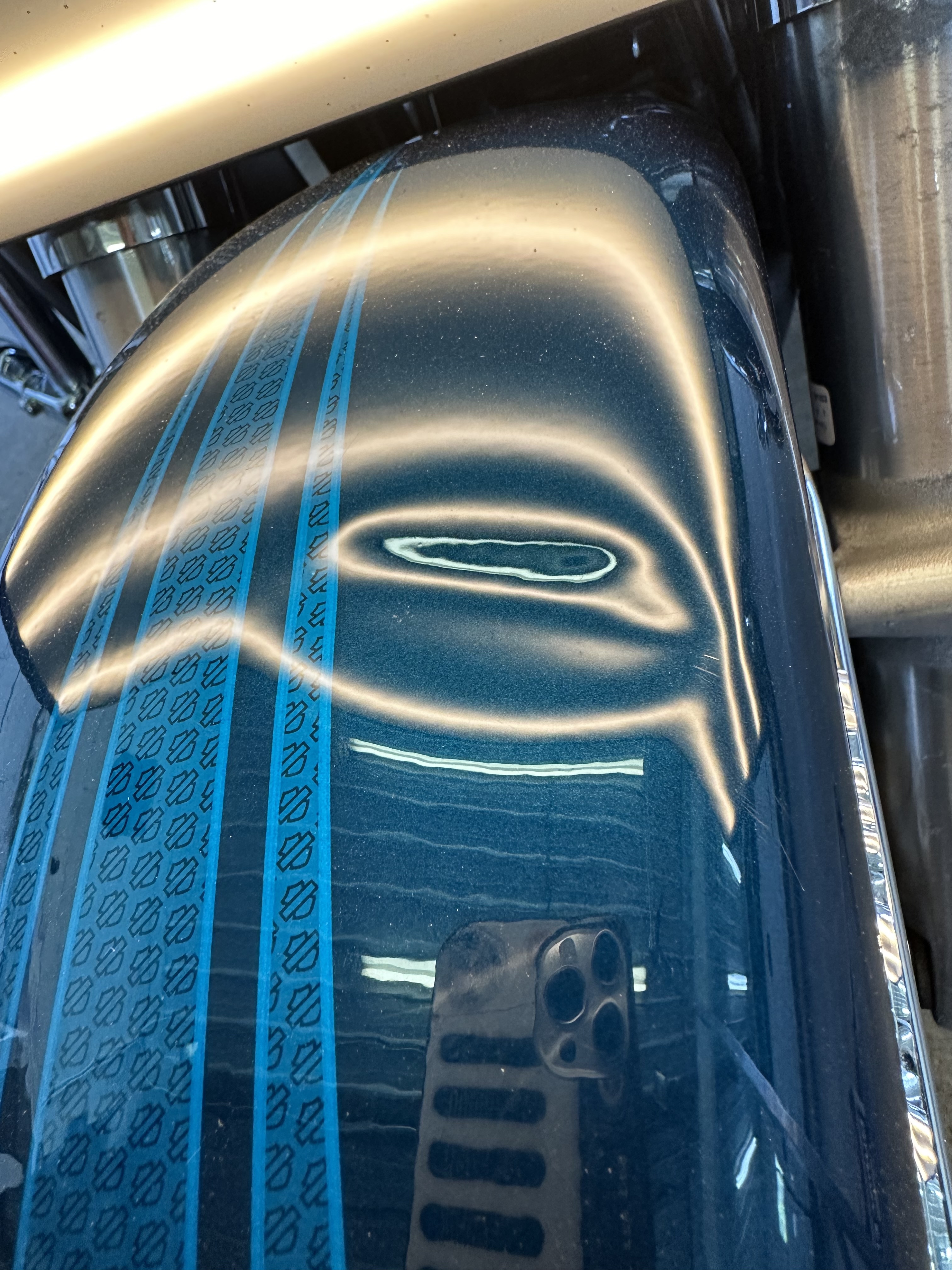 Car roof panel with large dent visible under inspection light before repair